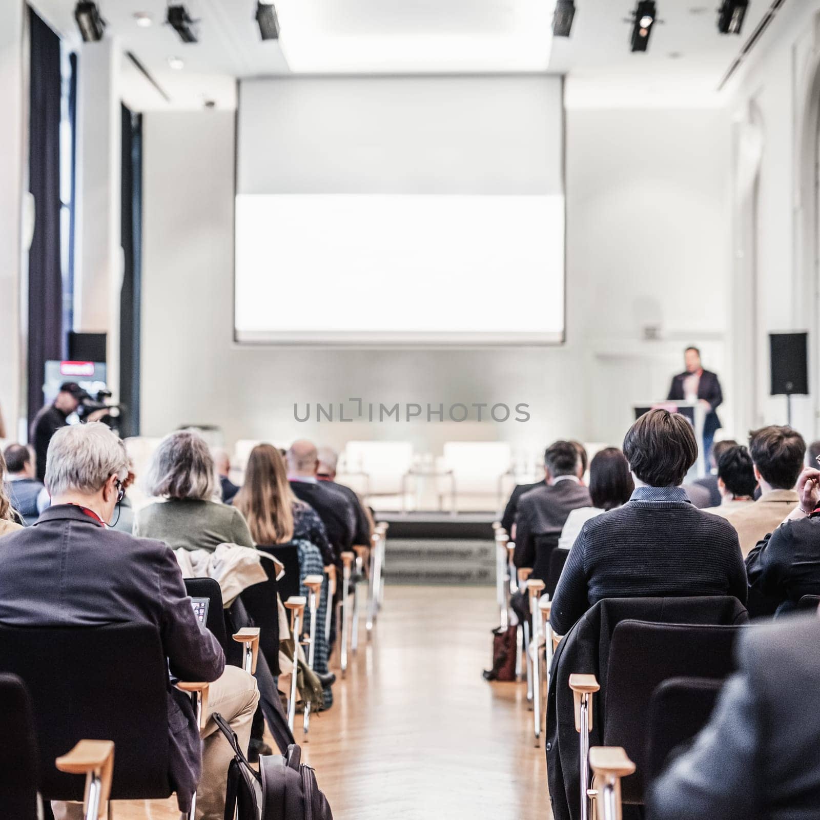 Speaker giving a talk in conference hall at business event. Rear view of unrecognizable people in audience at the conference hall. Business and entrepreneurship concept