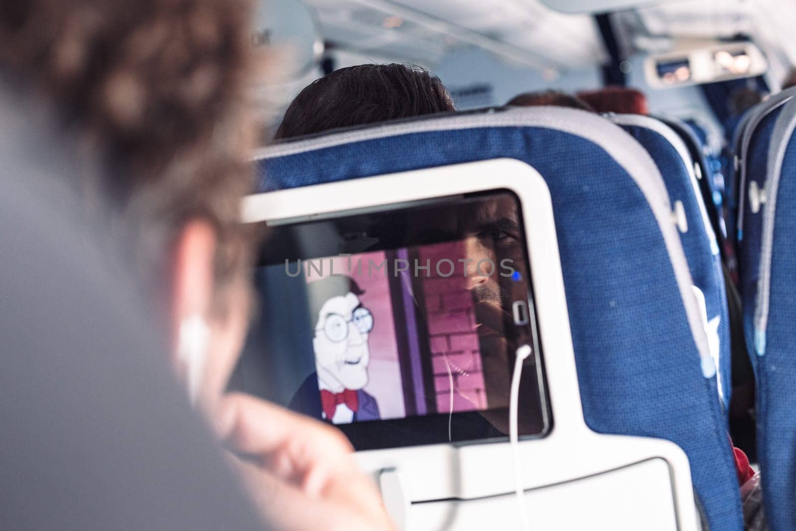 Reflection of a passenger on an airplane touch screen monitor while watching cartoon during long flight. Entertainment service system in aircraft