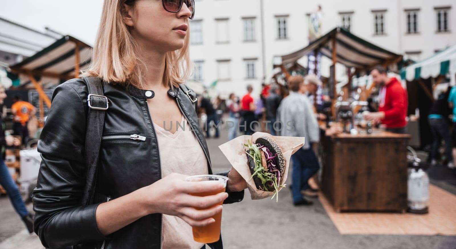 Close up of woman hands holding delicious organic salmon vegetarian burger and homebrewed IPA beer on open air beer an burger urban street food festival in Ljubljana, Slovenia