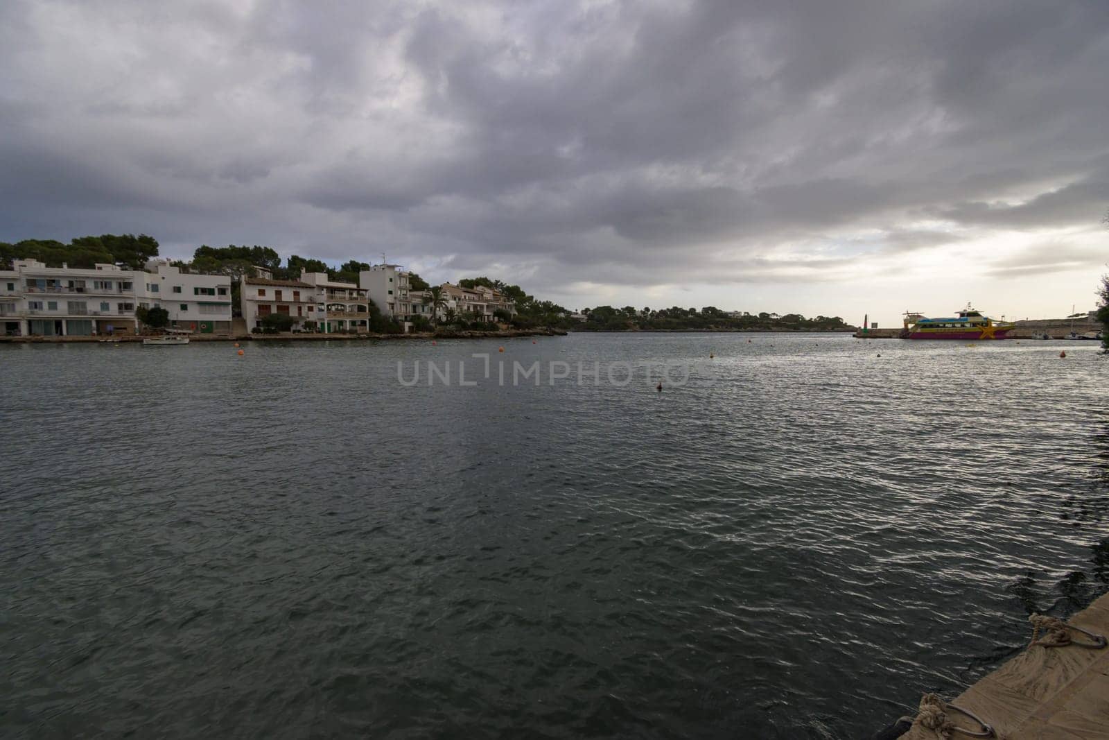 Coastal town under a gray, cloudy sky with dark water and overcast atmosphere, porto petro, mallorca balearic islands, spain
