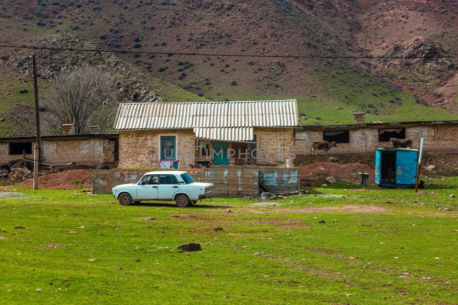 old classic soviet white sedan car in front of rustic farm house in Kyrgyzstan.