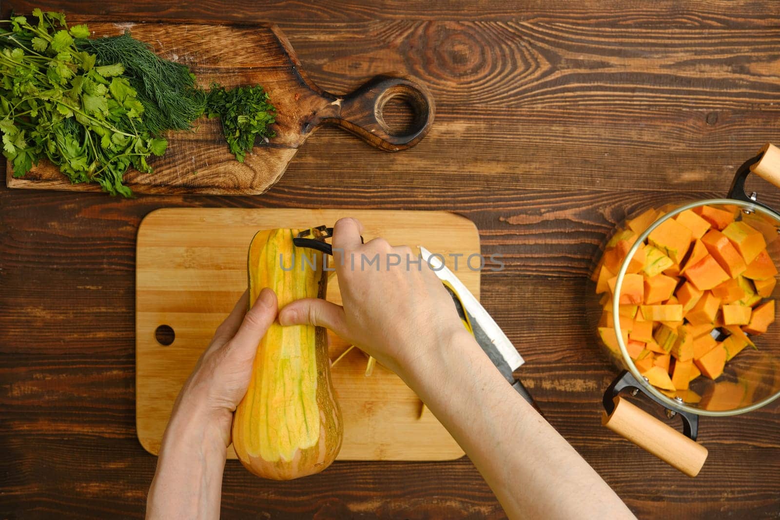 A person skillfully peels a butternut squash, surrounded by fresh herbs and diced squash. The warm wood tones of the kitchen create a welcoming atmosphere for cooking.