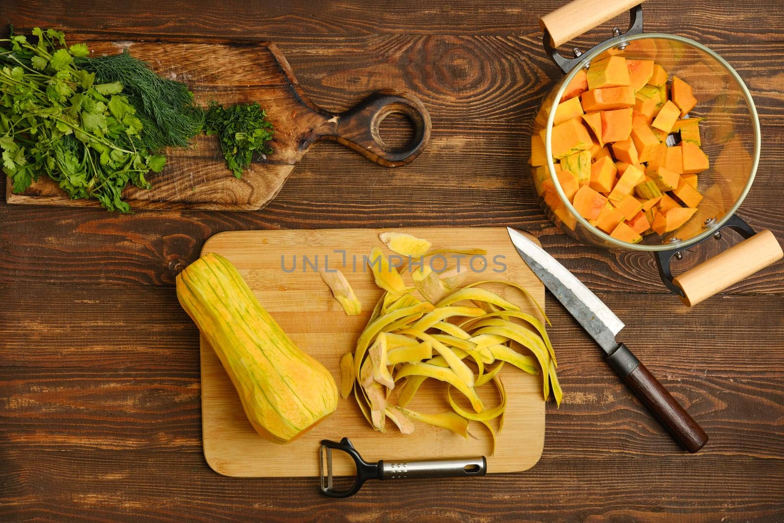 Fresh butternut squash is being peeled and chopped on a wooden cutting board, accompanied by vibrant herbs and tidy kitchen tools. The ambiance is bright and inviting, perfect for cooking.