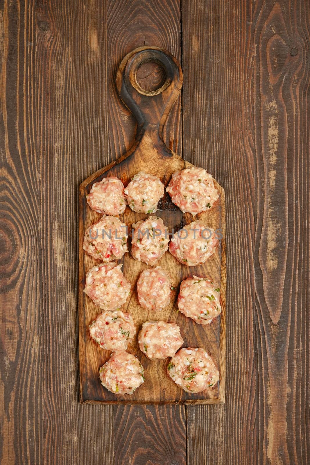 A wooden cutting board showcases a dozen freshly made meatballs, blending ground meat and herbs. The rustic texture of the board complements the delightful presentation in a warm kitchen setting.