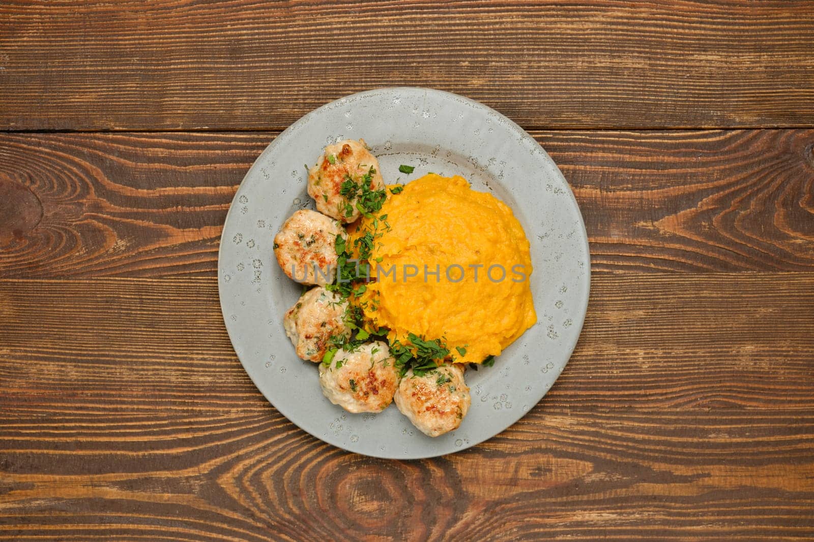 Top view of a plate with golden-brown meatballs garnished with herbs alongside a creamy mashed pumpkin