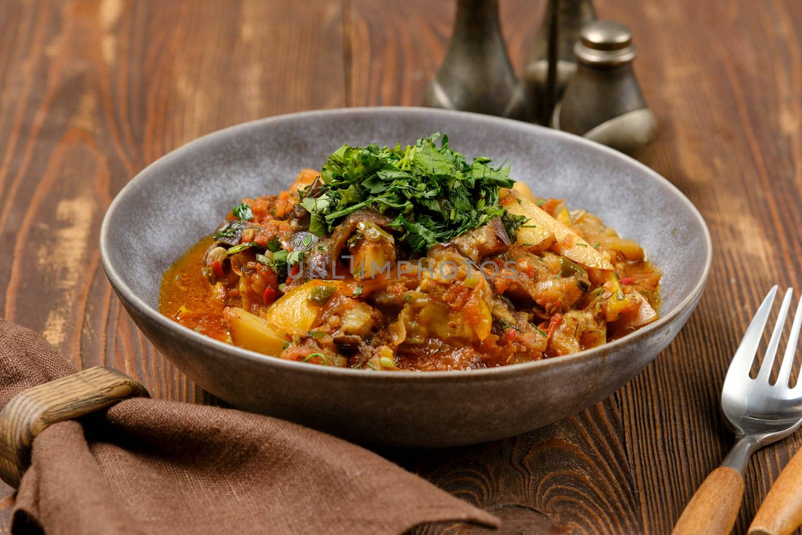 A flavorful vegetable curry fills a rustic bowl, garnished with fresh herbs. The dish is presented on a wooden table, creating a warm, inviting atmosphere perfect for a meal.