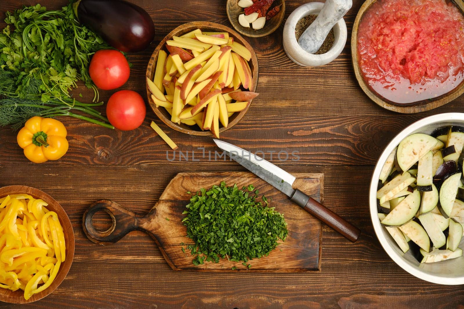 A vibrant assortment of fresh vegetables and herbs is spread across a wooden table. Herbs, tomatoes, and bell peppers are ready for chopping, showcasing the preparation for a nutritious dish.