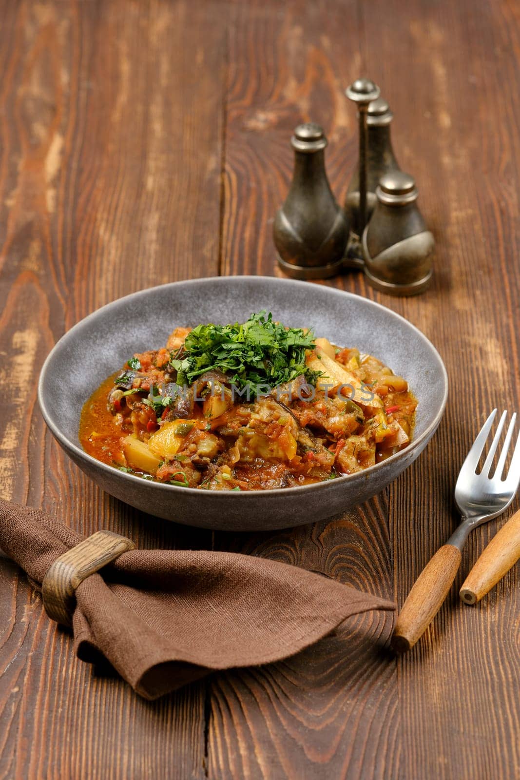 A flavorful Georgian vegetable stew is served in a bowl, garnished with fresh green herbs, on a rustic wooden table