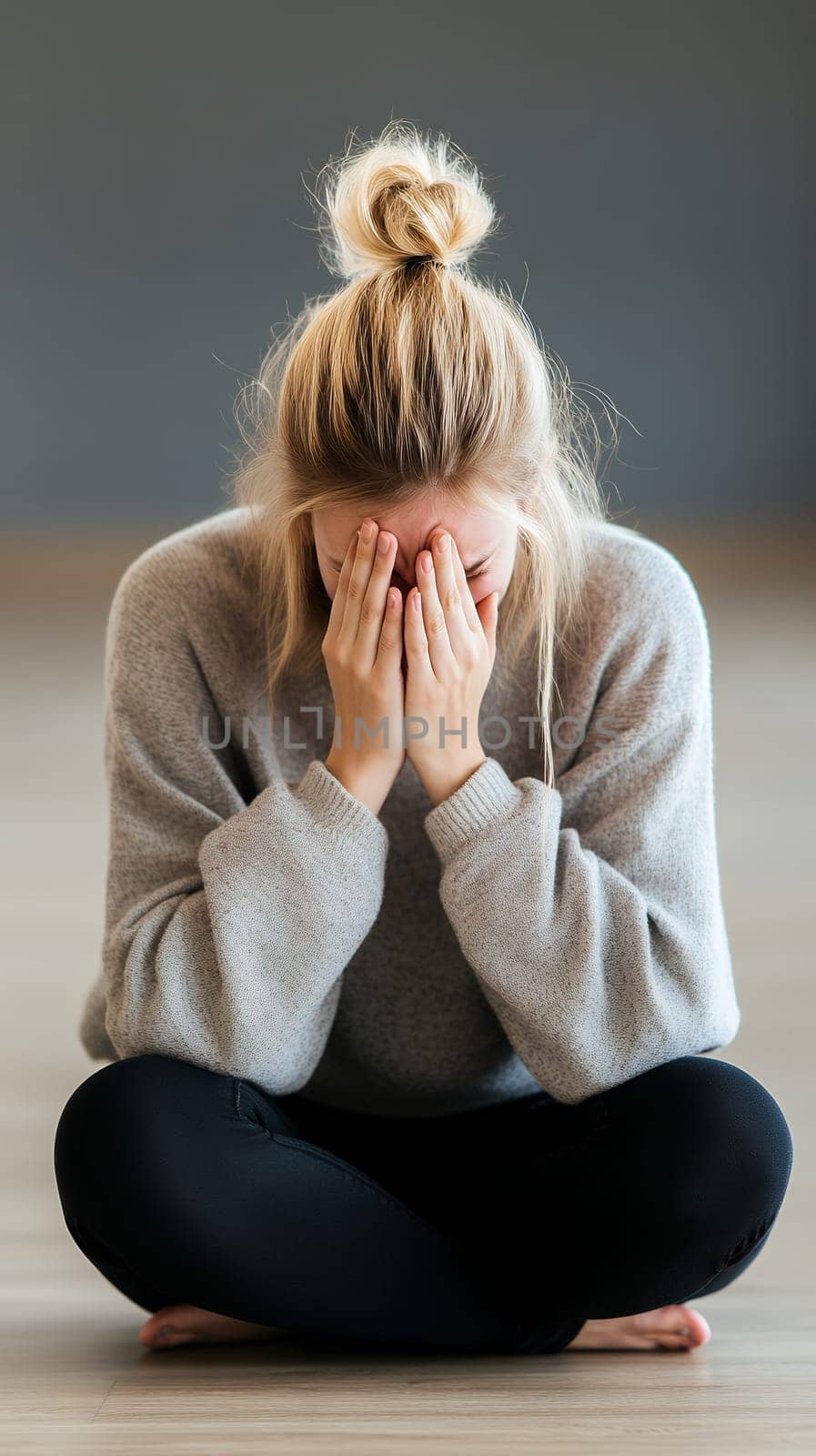 A woman sits cross legged, covering her face with her hands, conveying a moment of reflection and emotion.
