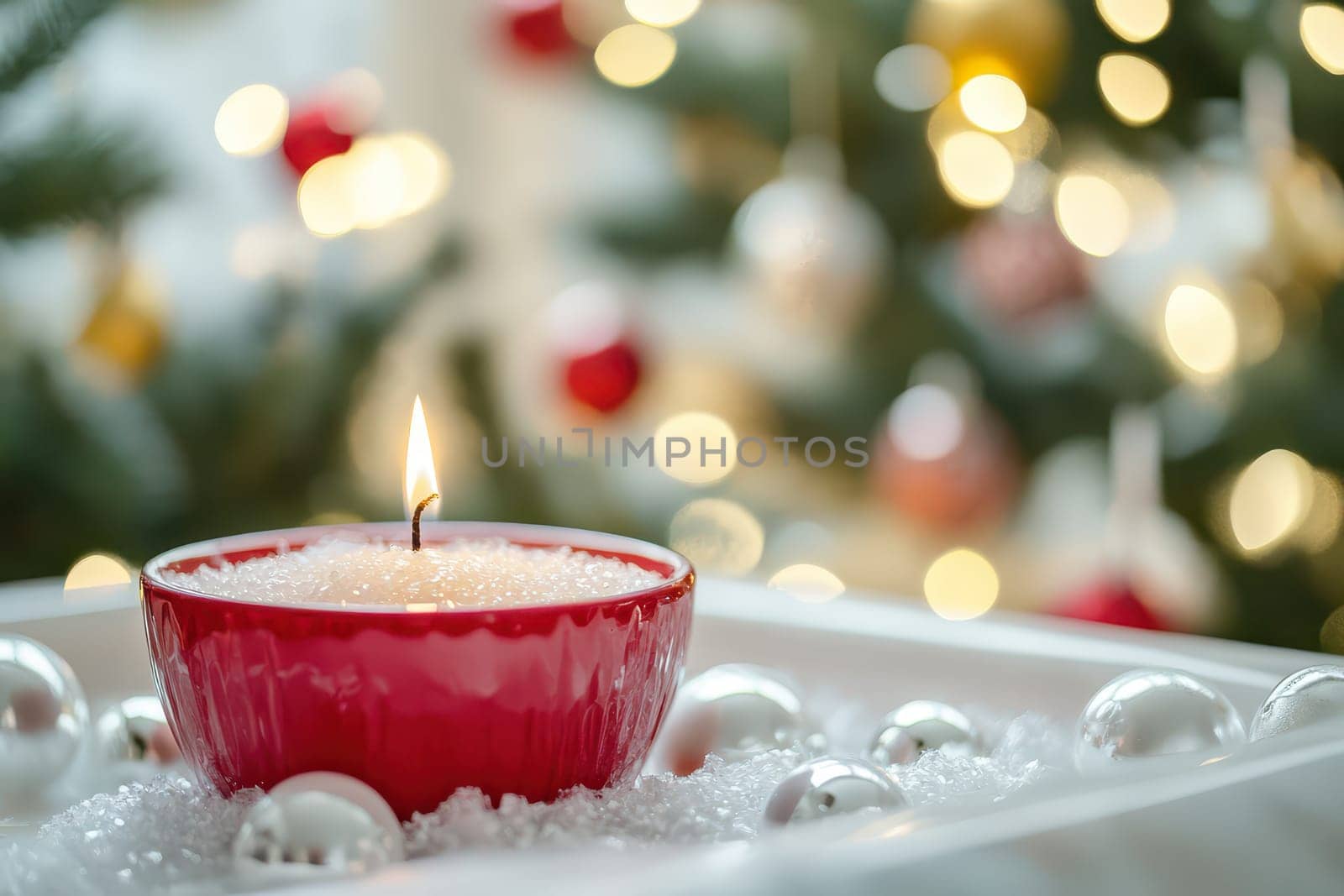 A vibrant red candle flickers gently in a decorative bowl surrounded by sparkling ornaments and a softly lit Christmas tree in the background.