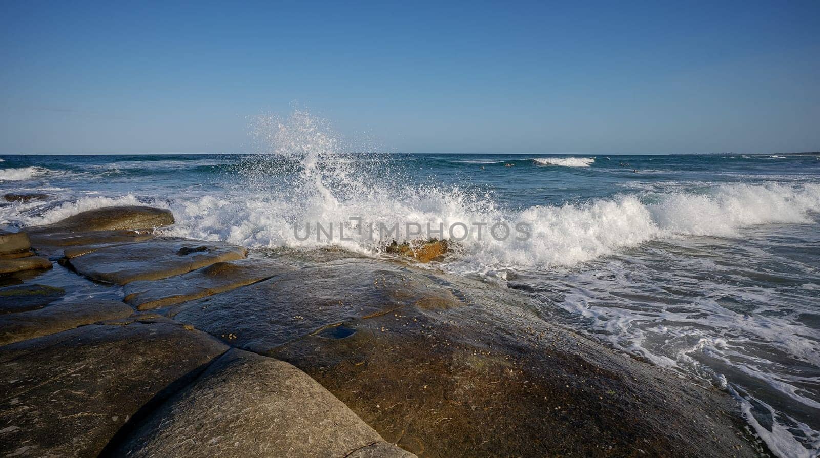 White foaming water splashes as surf waves break over large rock platform on the foreshore of the rocky headland at Point Cartwright, Kawana, Queensland
