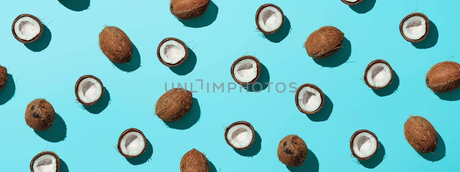 Creative layout of coconuts half on blue background. Tropical pattern, top view or flat lay. Hard light pop art minimal summer background. Horizontal banner