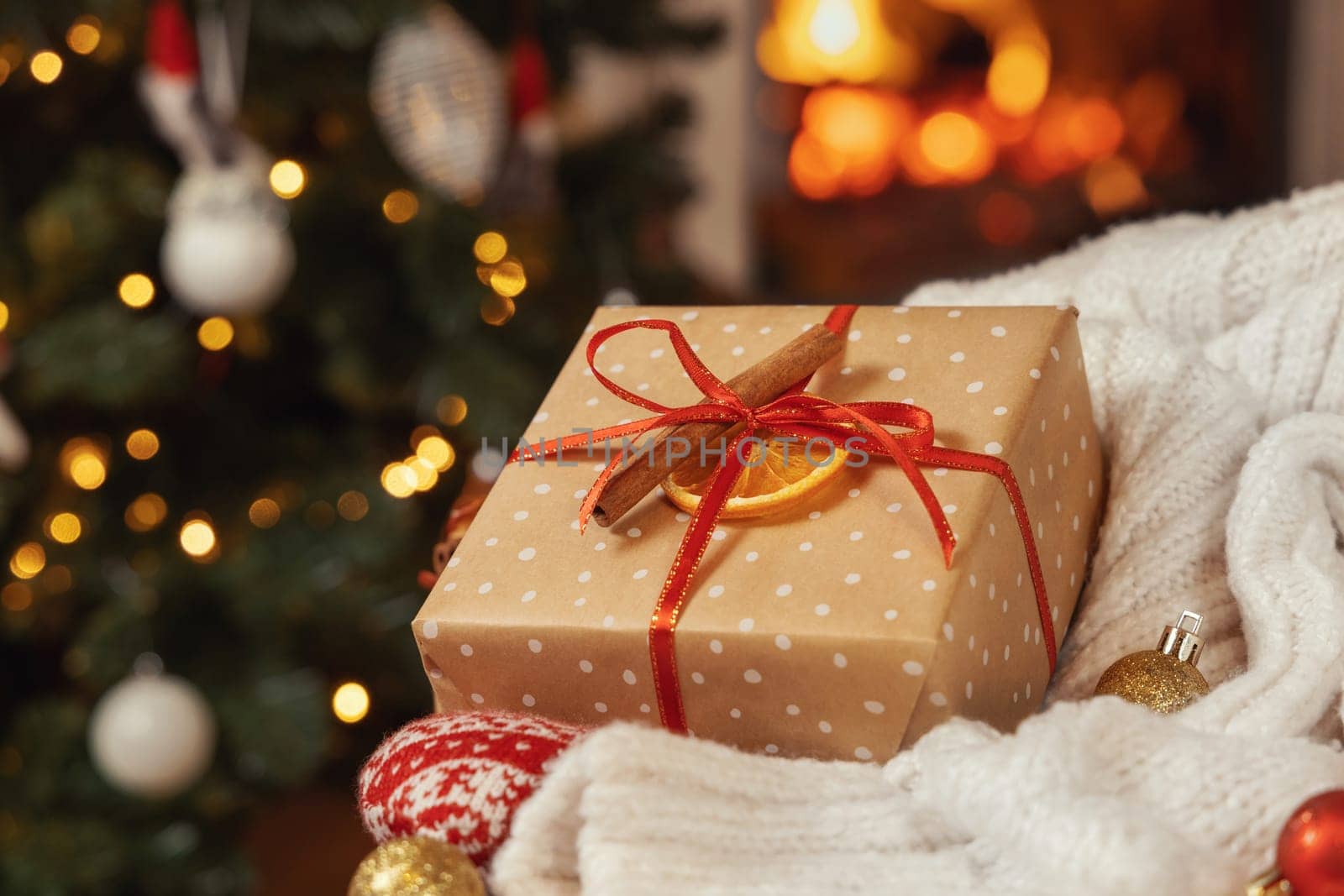 Christmas gift with bow near white sweater against burning fireplace and christmas tree lights. Warm winter family atmosphere, Magical Holiday time