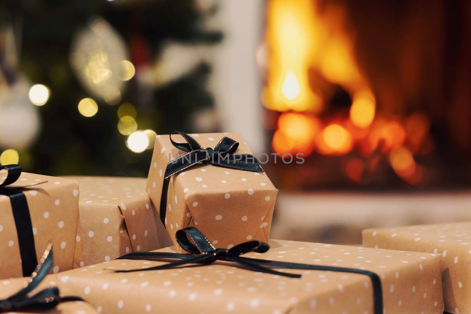 Wrapped Christmas gifts with black ribbon bows against burning fireplace and christmas tree decorated with lights. Warm winter family atmosphere, Magical Holiday time