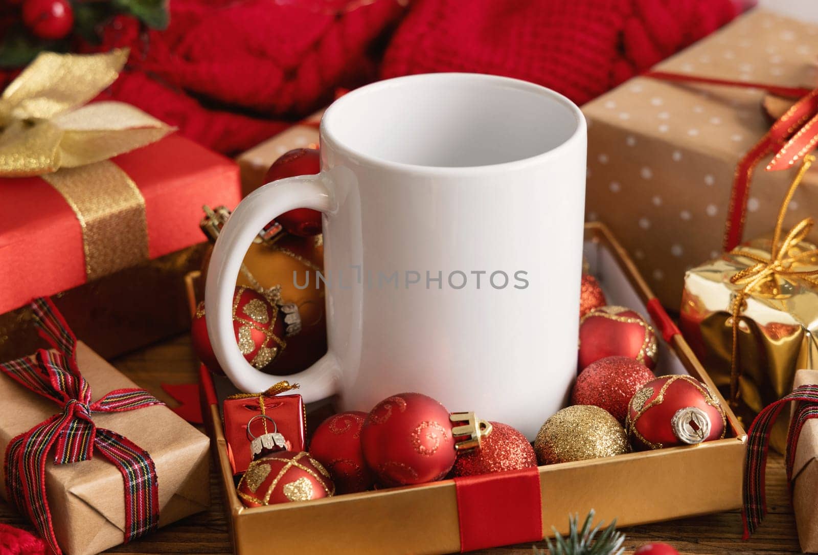 White blank coffee mug near white knitted sweater, wooden Christmas decor and lights, copy space. Winter atmospheric mock up in rustic or scandinavian style