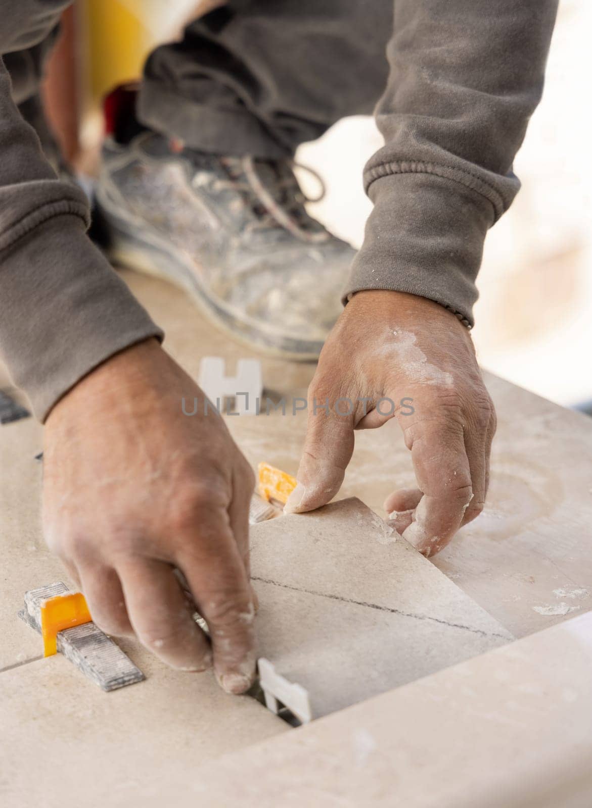 Tiler laying the ceramic tile on the floor with dusty hands closeup. Ceramic tiles and tools for tiler. Professional craftman during home renovation or construction new house
