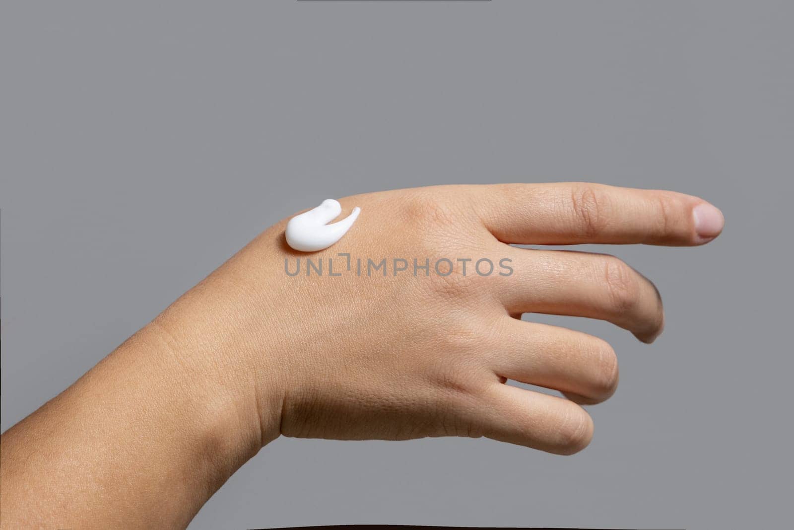 Drop of white moisturizing cream on female hand closeup against grey. Beauty treatment or handcare procedure in a spa salon. nice natural short nails. .