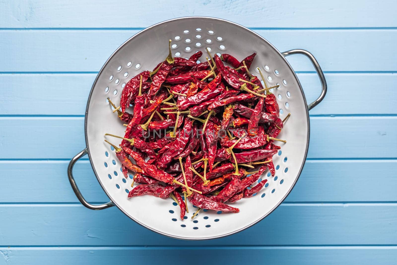 Dried red chili peppers in colander on a blue table. Top view.