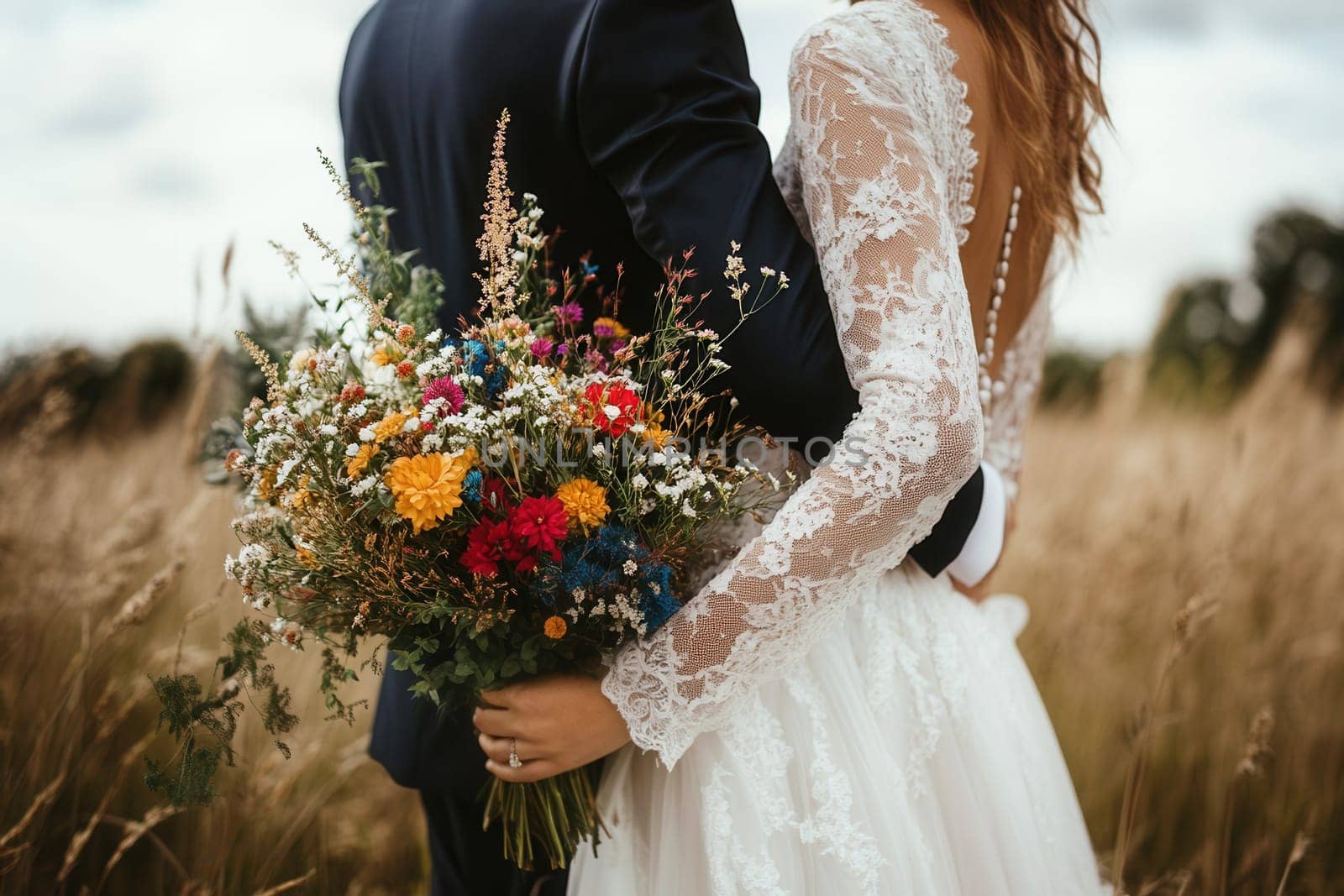 Newlywed couple embracing in a field, holding a vibrant bouquet of wildflowers