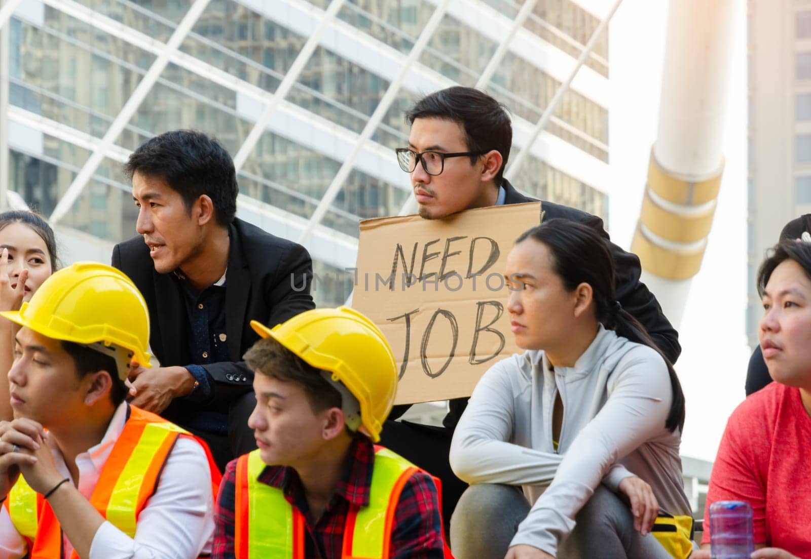 Group of Asian people in different career protesting and raising banners in the city for justice and equal rights . A man in black suit holding a sign of NEED JOB, demonstration concept.