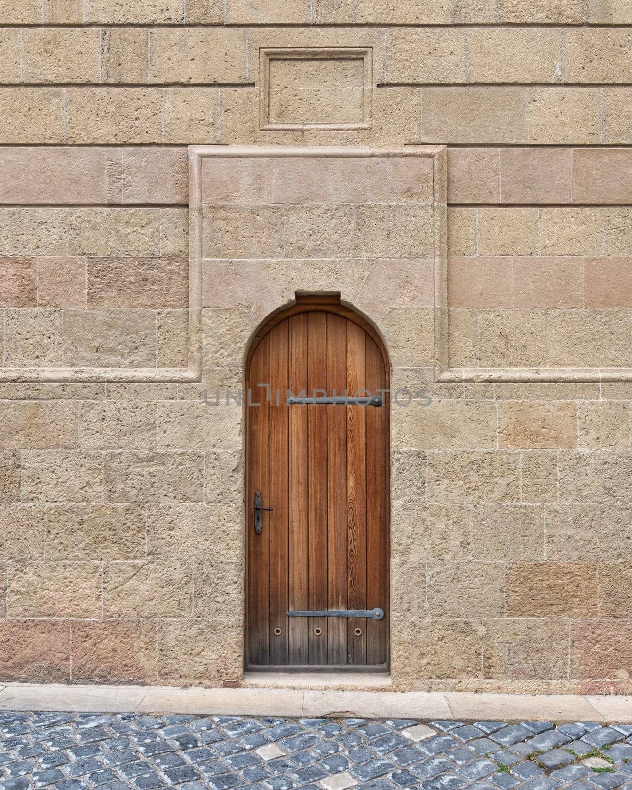 A weathered wooden door stands closed against a textured stone wall, framed by soft hues of beige and gray on a Cobblestone Street in a Historic Area
