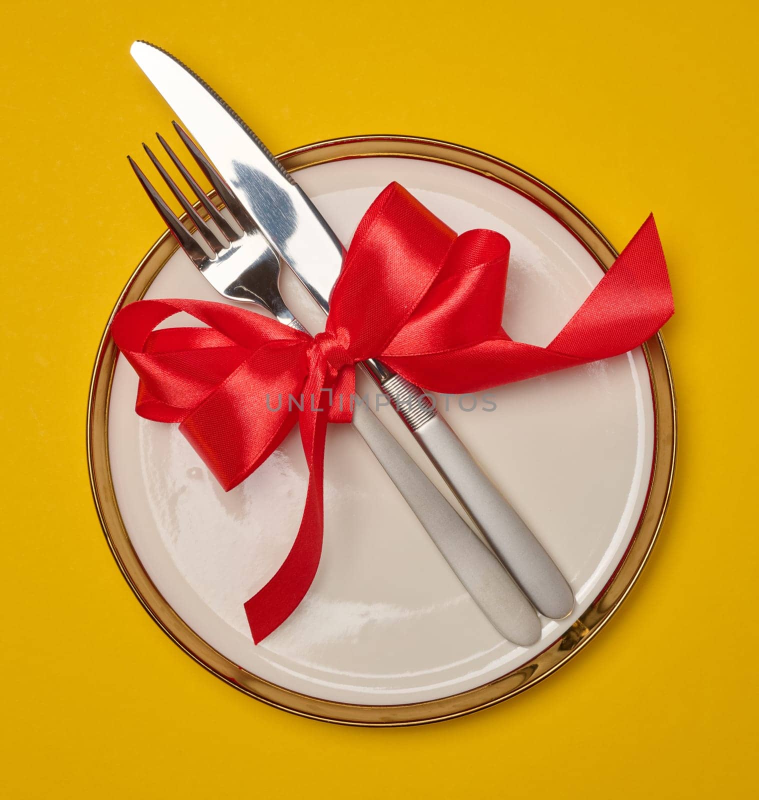 Round white plate and tied with red bow view with knife on yellow background, festive table setting