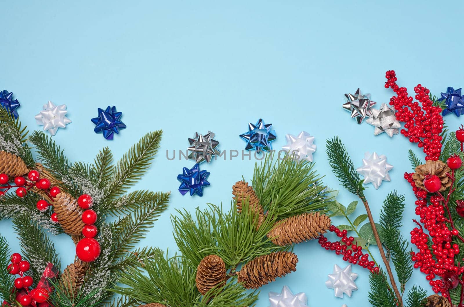 Decorative Christmas branch with red berries and pine cones on a blue background, top view. Copy space