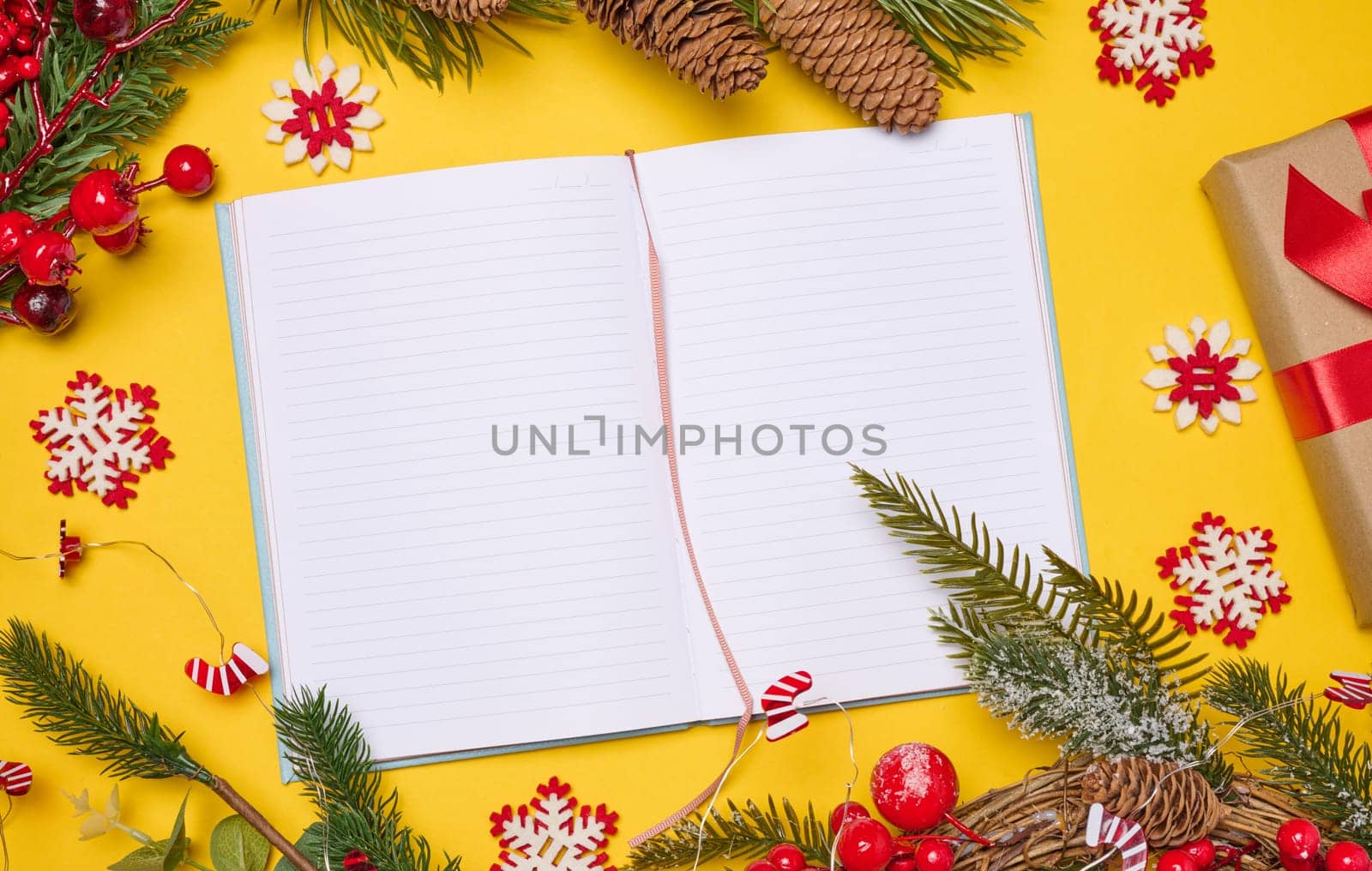 Open notebook with empty blank sheets on yellow background with Christmas decor, top view