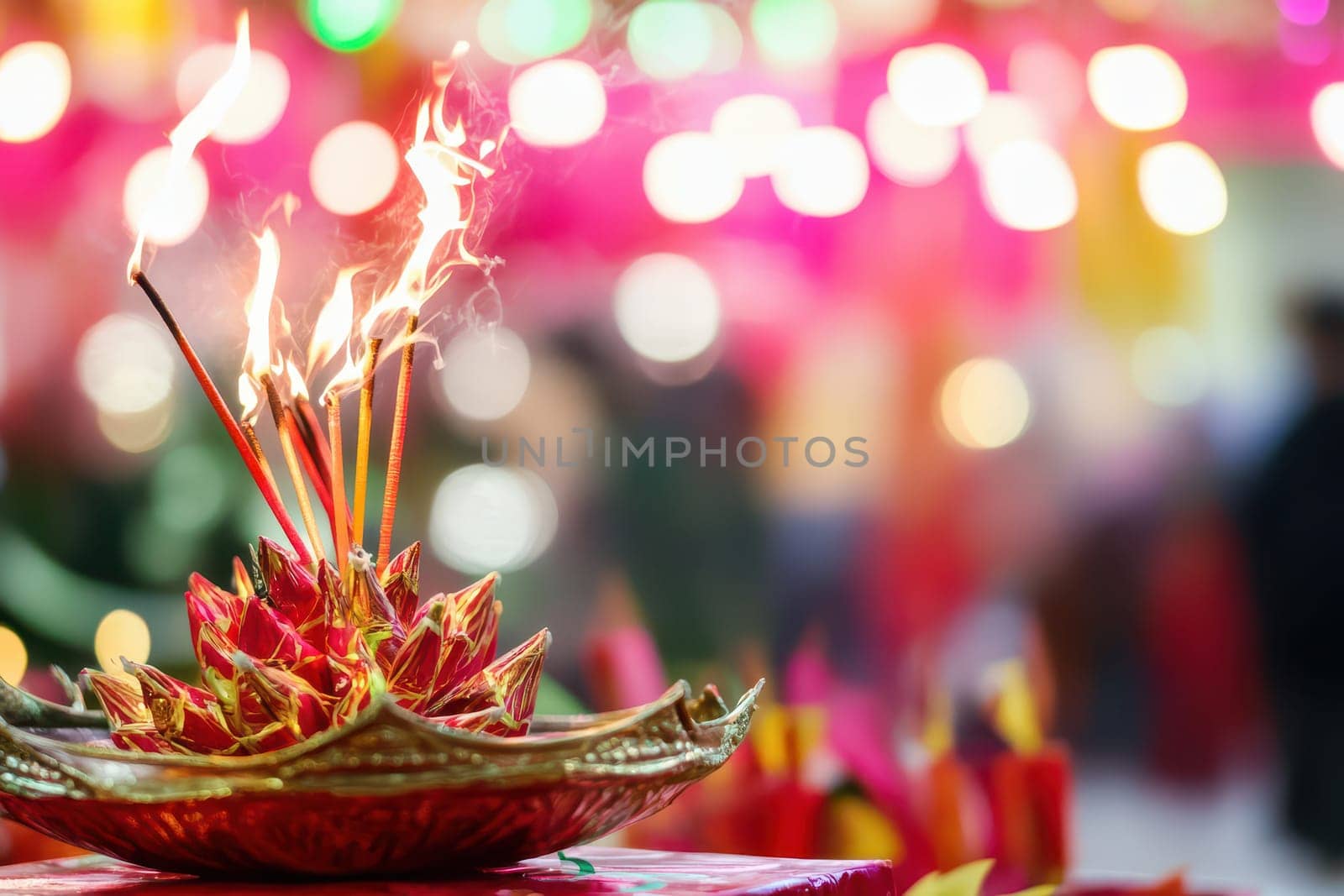 Incense sticks burn brightly atop a decorative holder surrounded by colorful lights and decorations in a vibrant celebration setting.