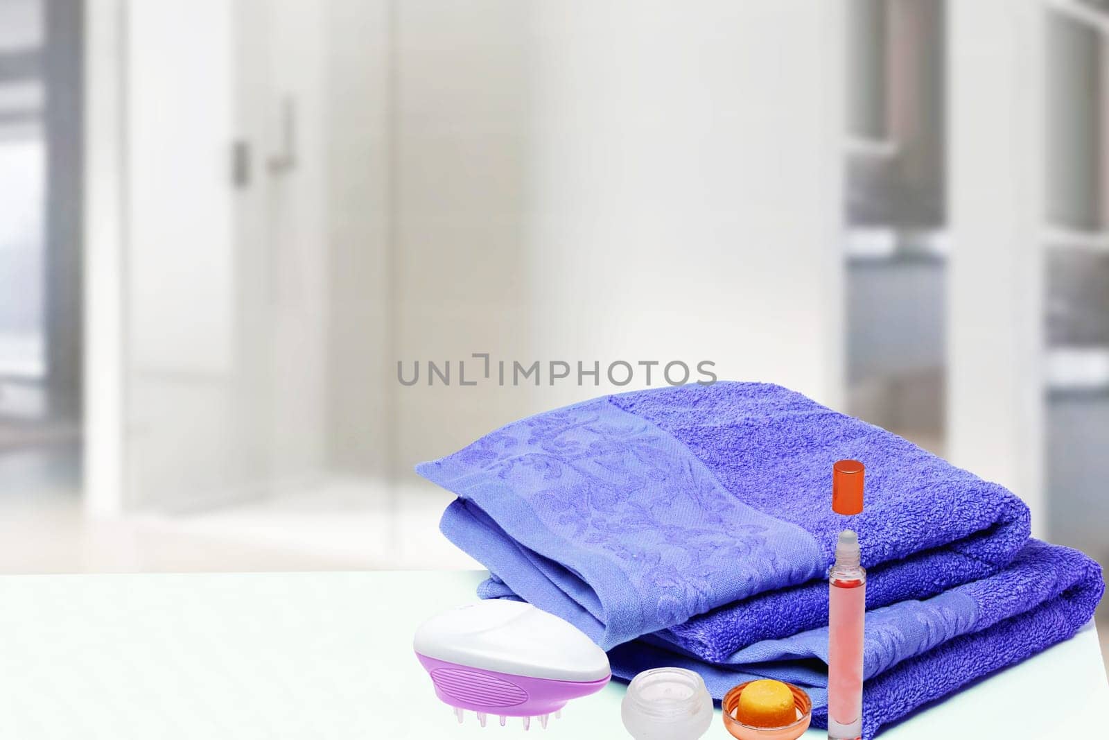 Table top on towels background. Closeup of fresh soft terry bath towels with massage brush, cosmetic cream and soap bottle over blurred bathroom background. Space.