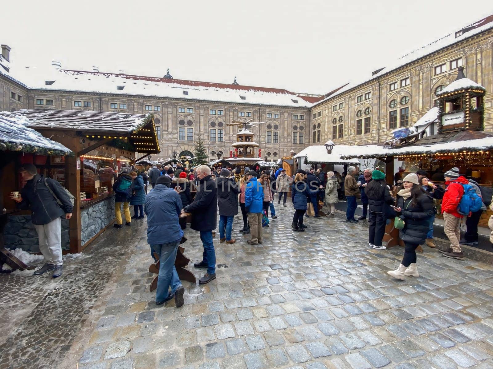 Munich, DE, Dec. 19 2022  People exploring the festive Christmas market in the snowy courtyard of the Munich Residenz, surrounded by decorated stalls and holiday lights