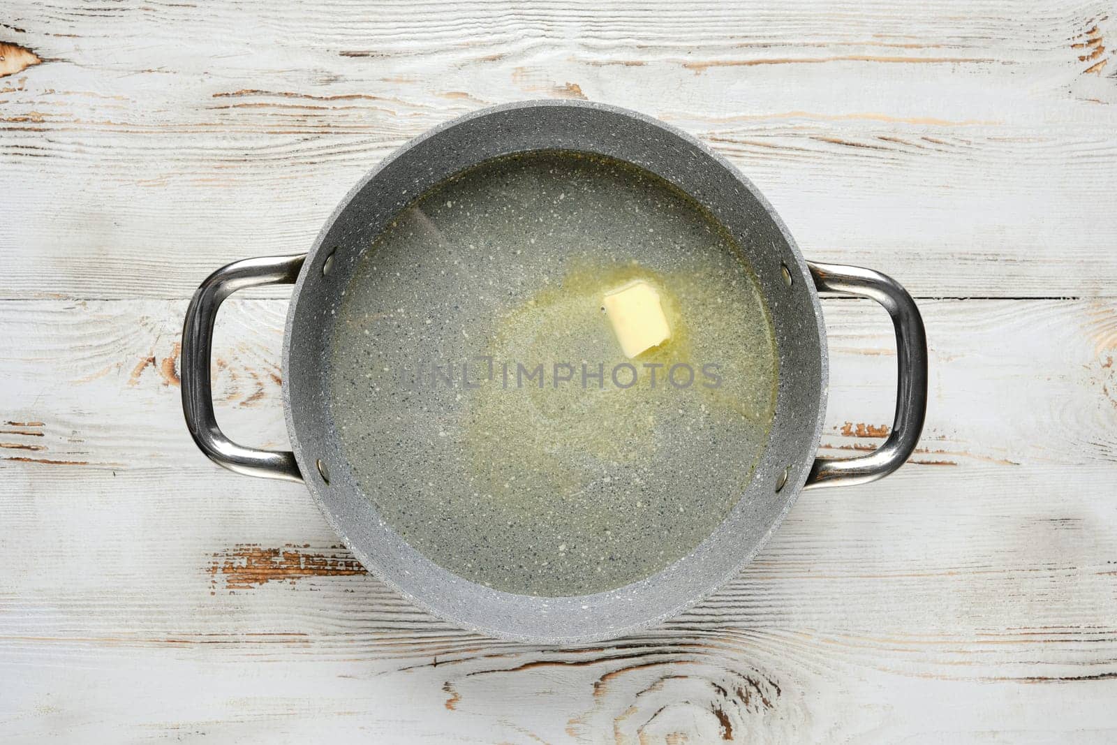 Overhead view of a piece of butter melts in a pan on a wooden table