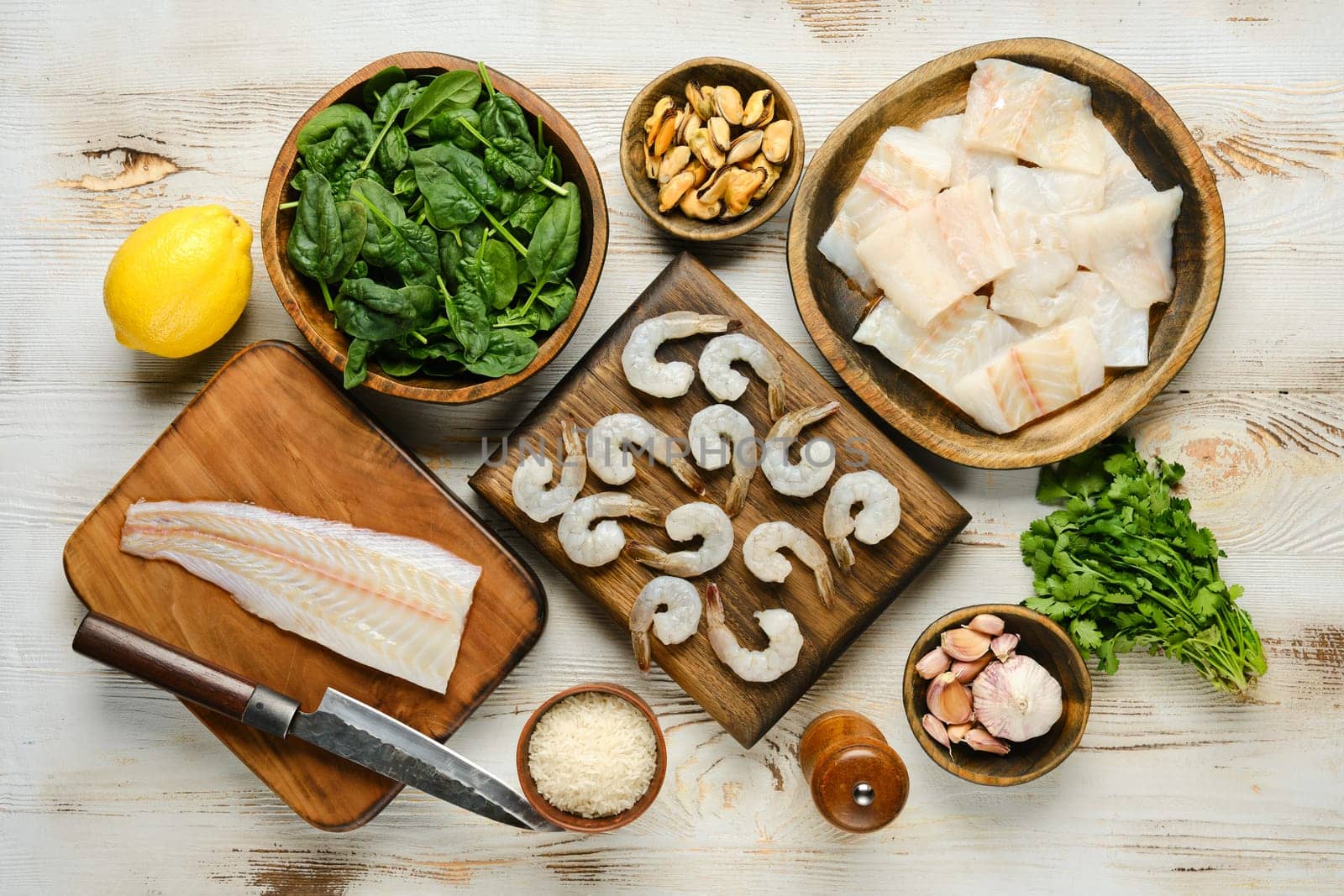 Top view of fresh ingredients including shrimp, fish, spinach, lemon, and mussels arranged on wooden boards
