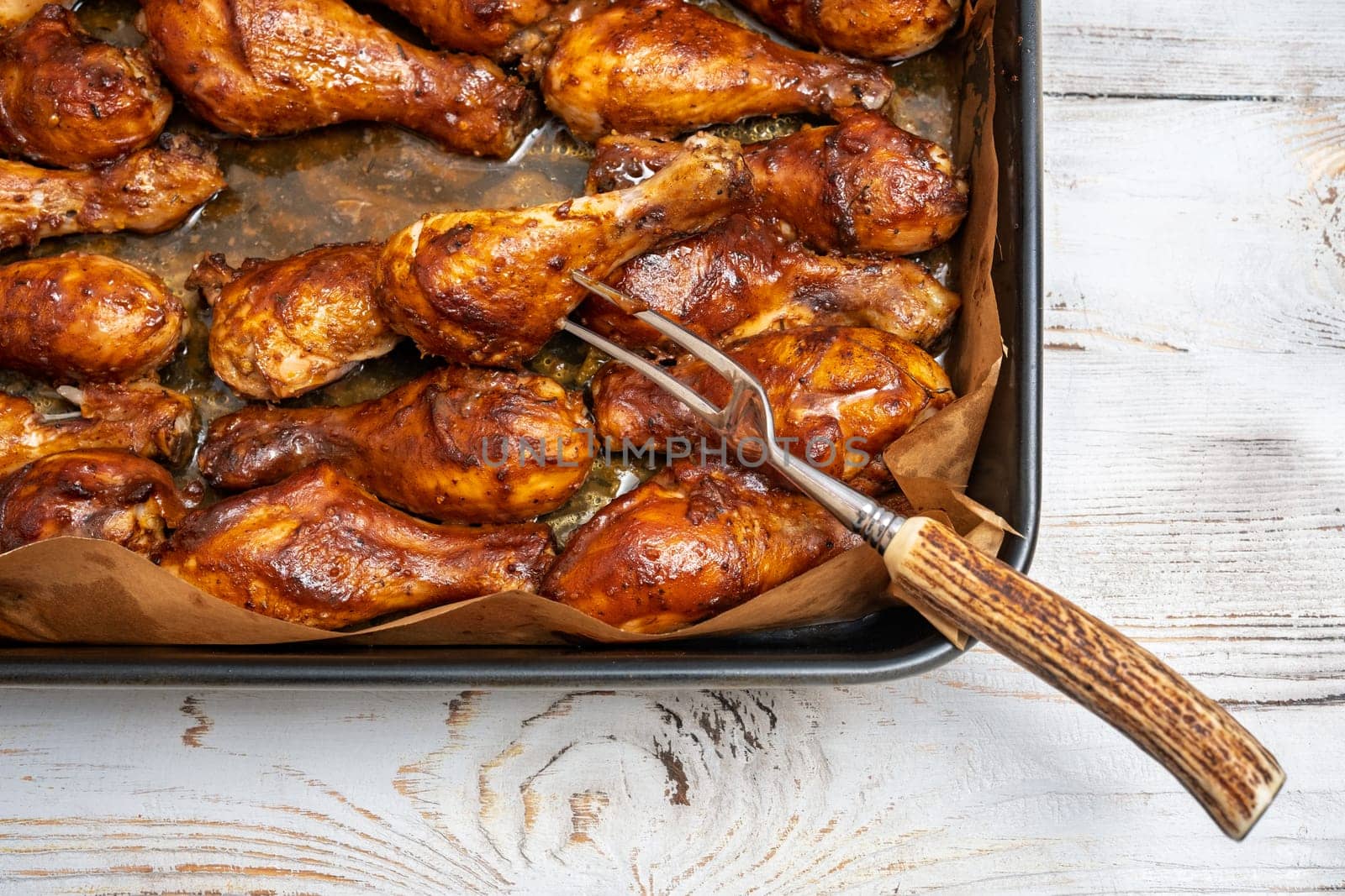 A baking tray filled with perfectly roasted chicken drumsticks glistening with a rich glaze on a rustic wooden table. A fork rests on the side, ready to serve the delicious meal.