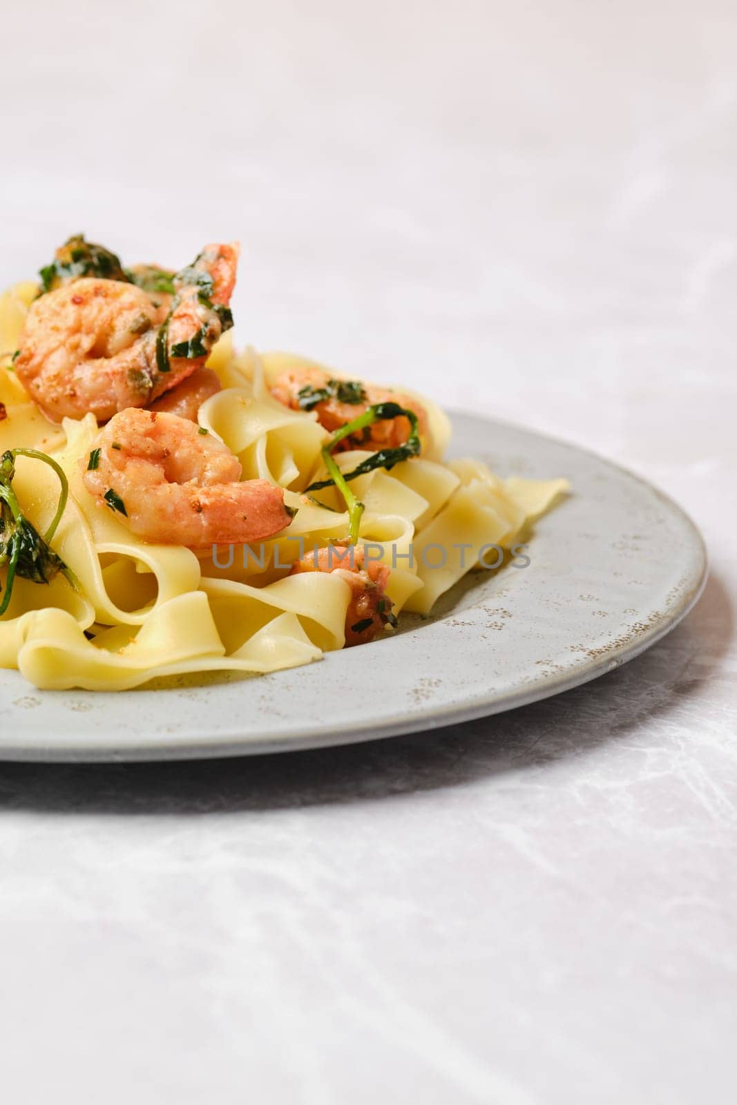 A serving of shrimp fettuccine garnished with fresh herbs is elegantly presented on a gray plate, showcasing a delightful blend of flavors and colors, perfect for a special meal or family dinner.