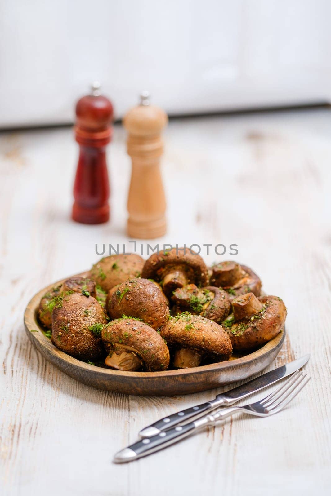 A wooden plate with crispy golden mushrooms, garnished with herbs. Two decorative pepper shakers stand in the background, adding to the inviting atmosphere of the dining table.