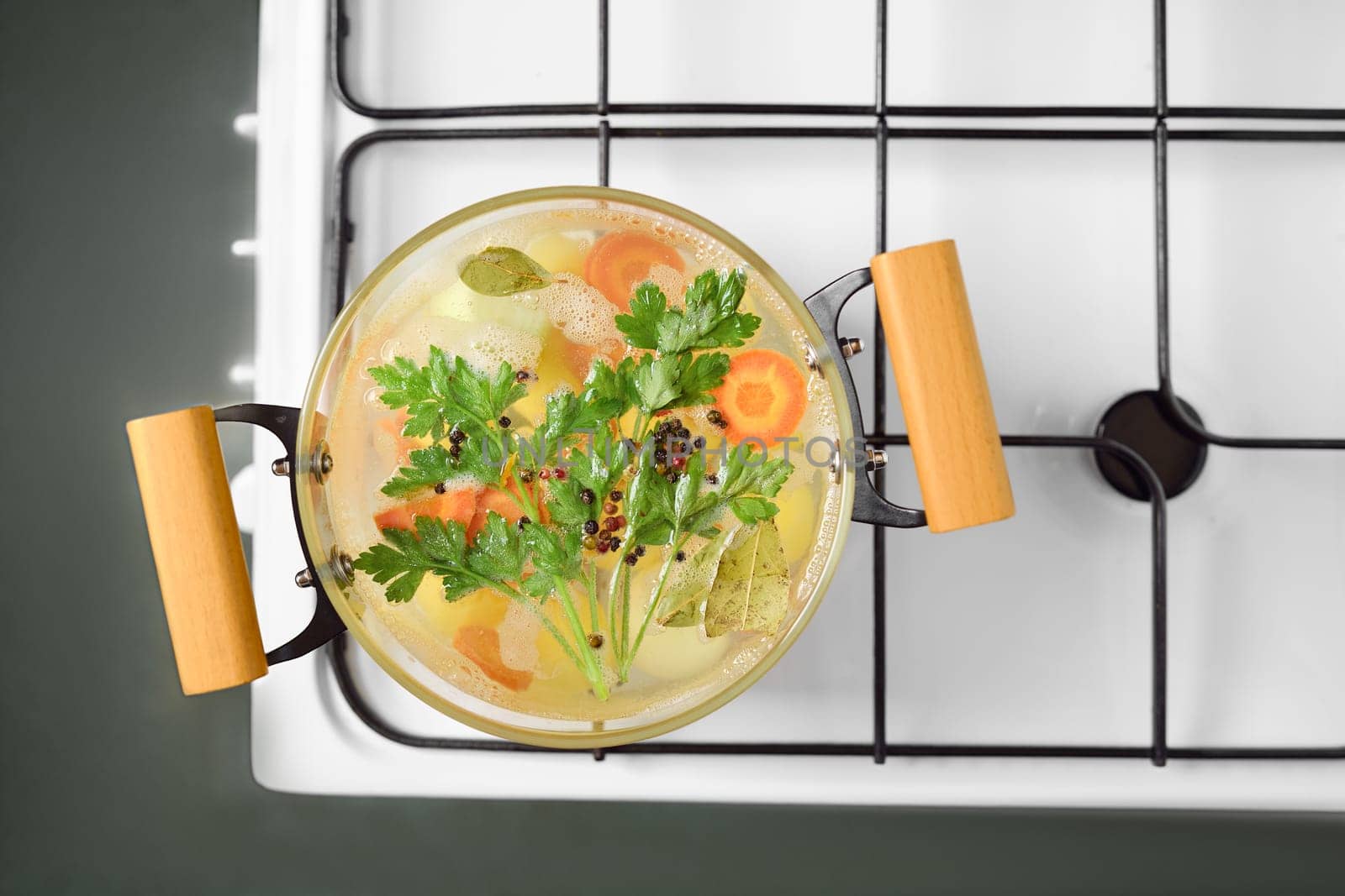 A pot of simmering vegetable broth filled with assorted fresh carrots, potatoes, herbs, and spices rests on a stovetop. The vibrant colors and aromas create a warm, inviting atmosphere for cooking.