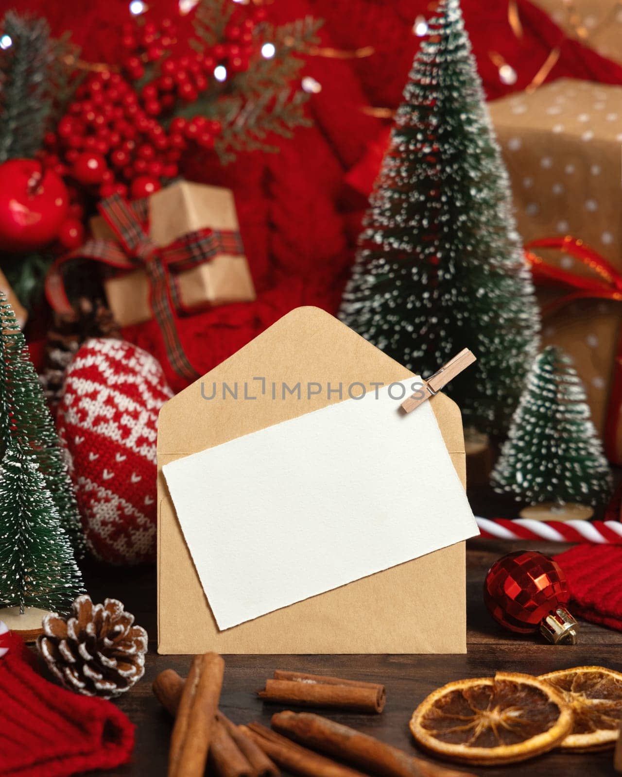 White postcard and craft envelope near Christmas decor, trees, spices and red knitted sweater on wooden table closeup, copy space. Winter atmospheric mock up, holiday greeting