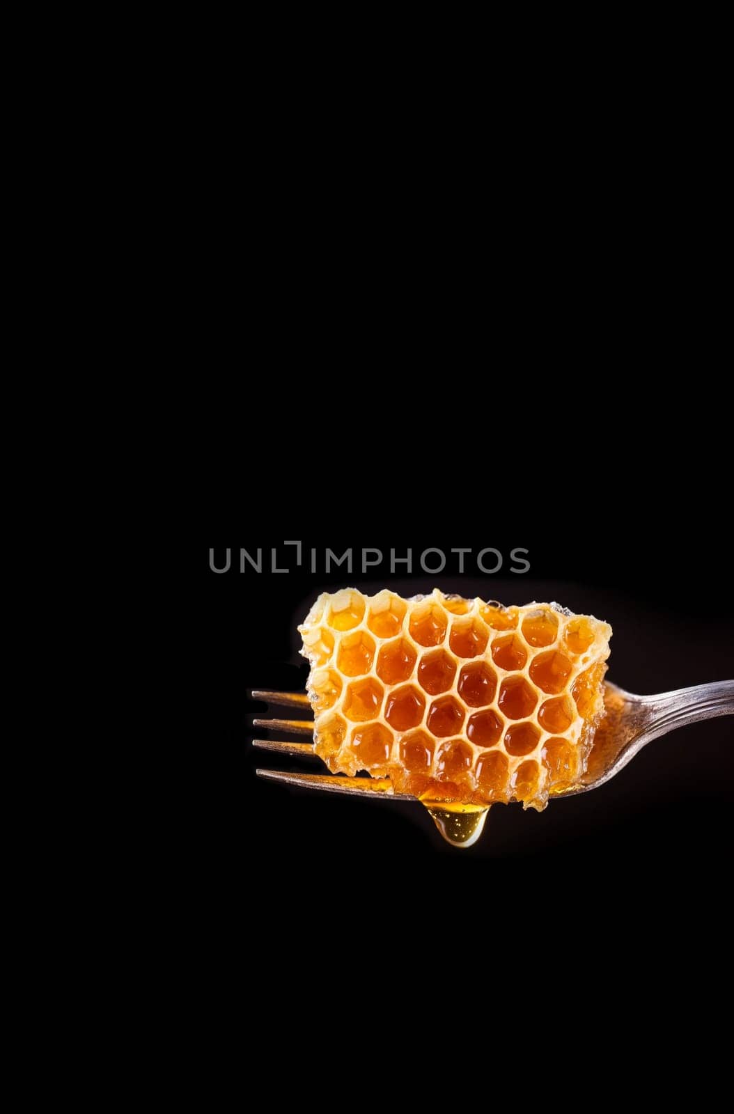 honeycomb on an antique fork. The honeycomb glistens with honey, and a few drops noticeably flow down. on a black background