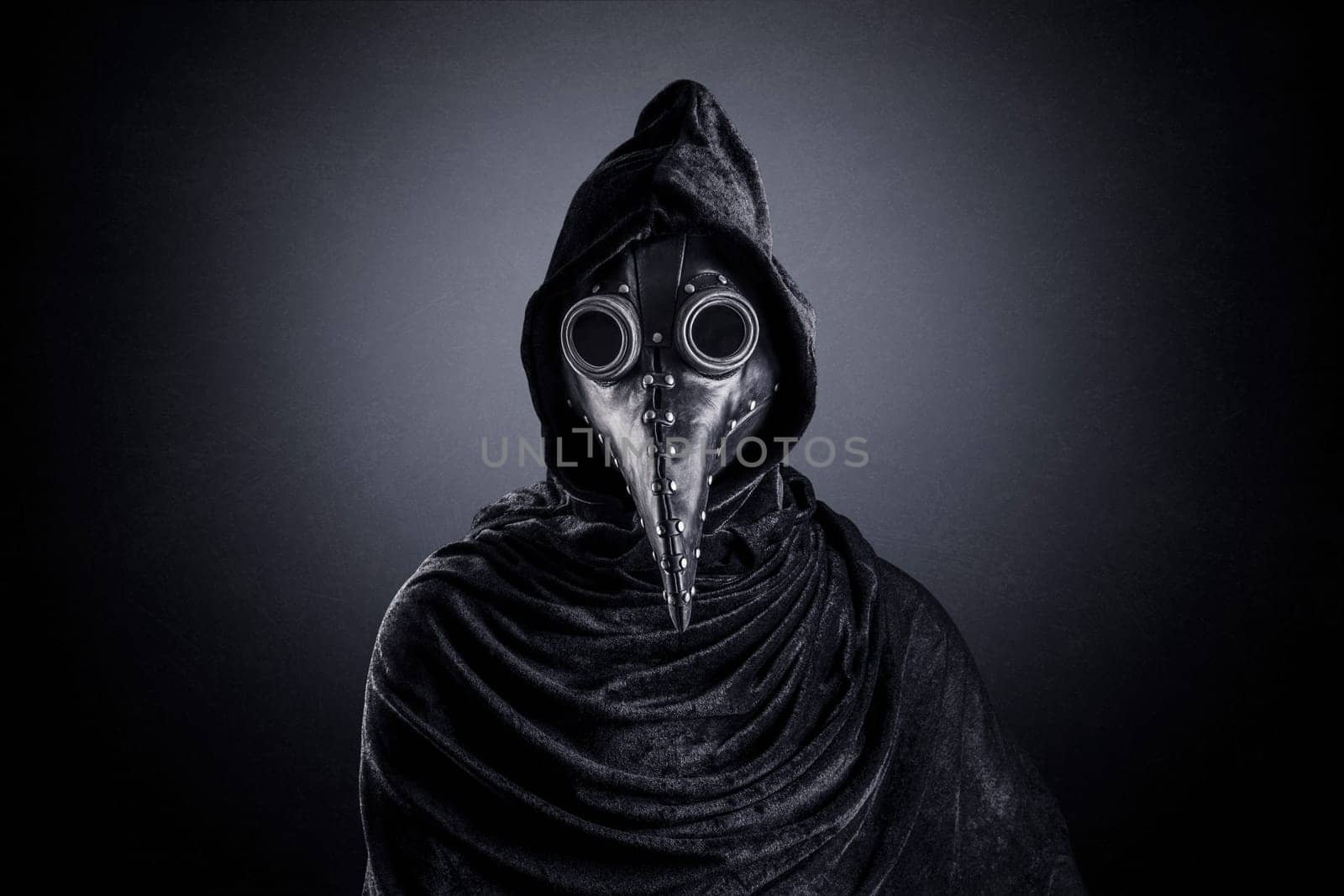 Plague doctor in hooded cloak at night over dark misty background