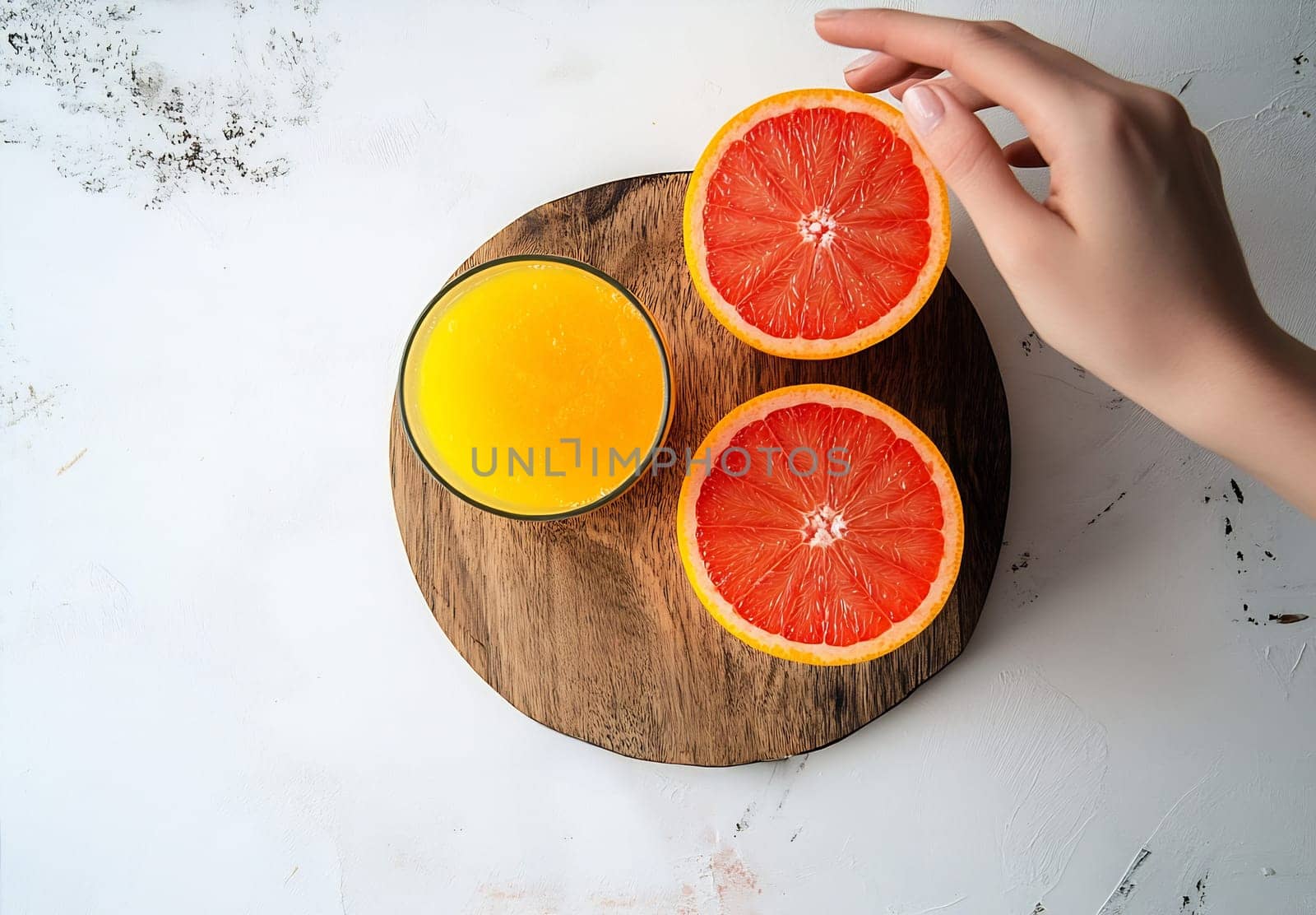 A hand reaches for a slice of bright orange grapefruit beside a glass of fresh orange juice on a wooden platter.