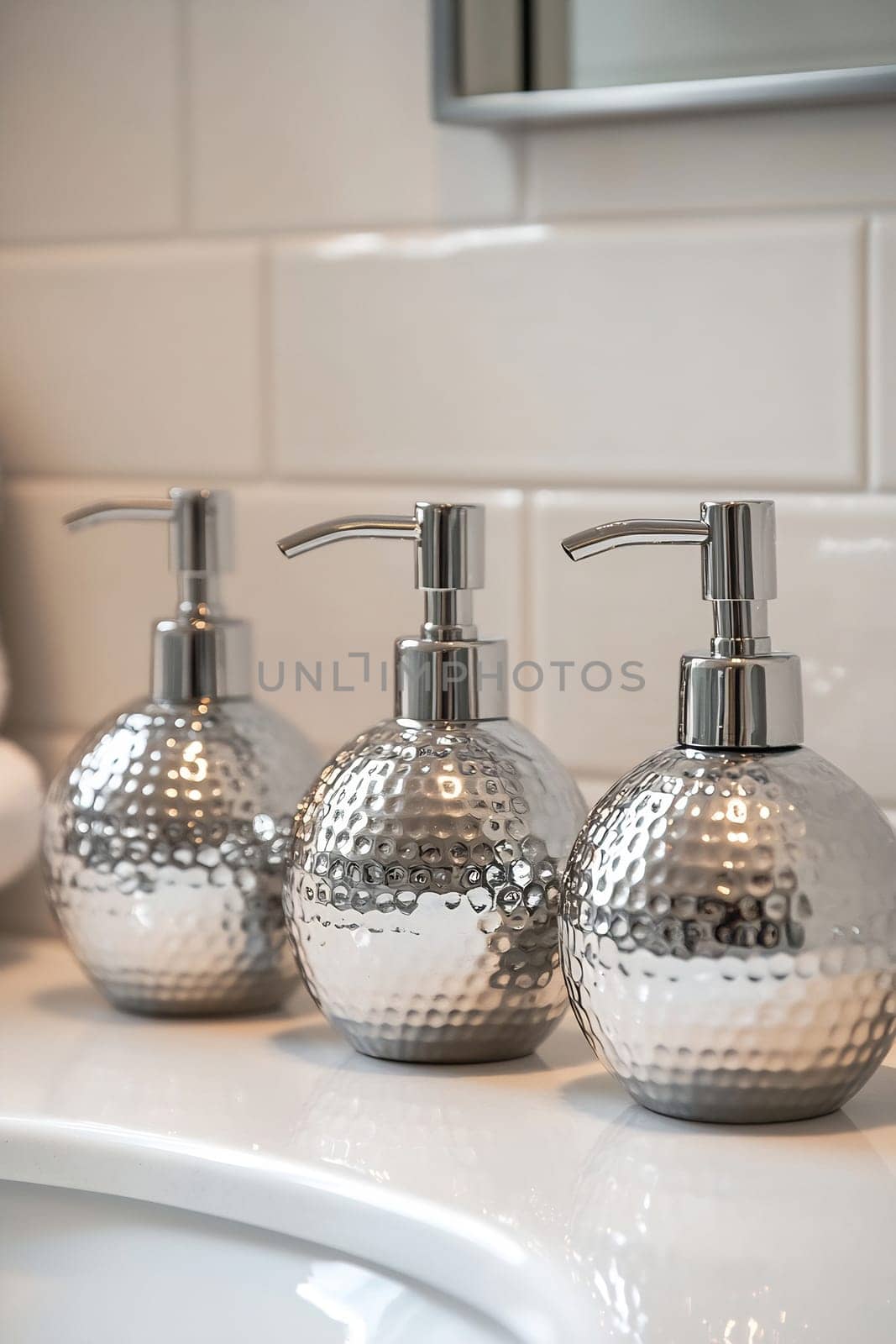 Three elegant silver soap dispensers with a hammered finish sit on a bathroom sink, adding a modern touch to the decor.
