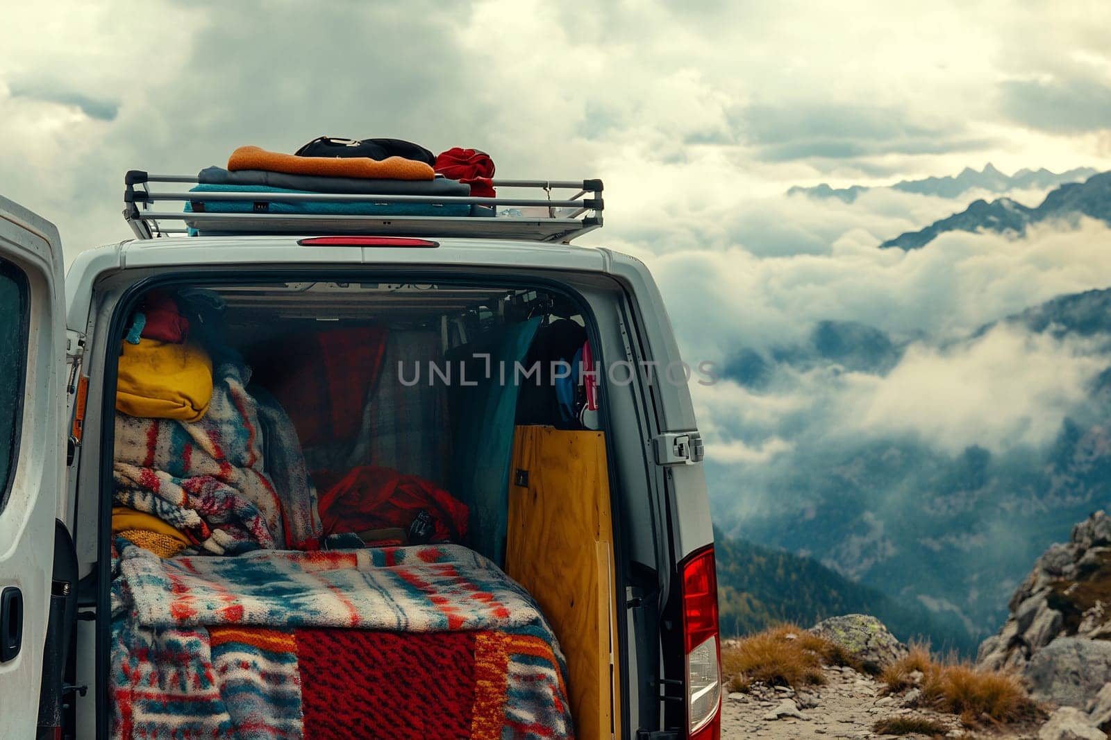 Inside a van, colorful blankets and pillows create a cozy atmosphere while mountains and clouds fill the background.