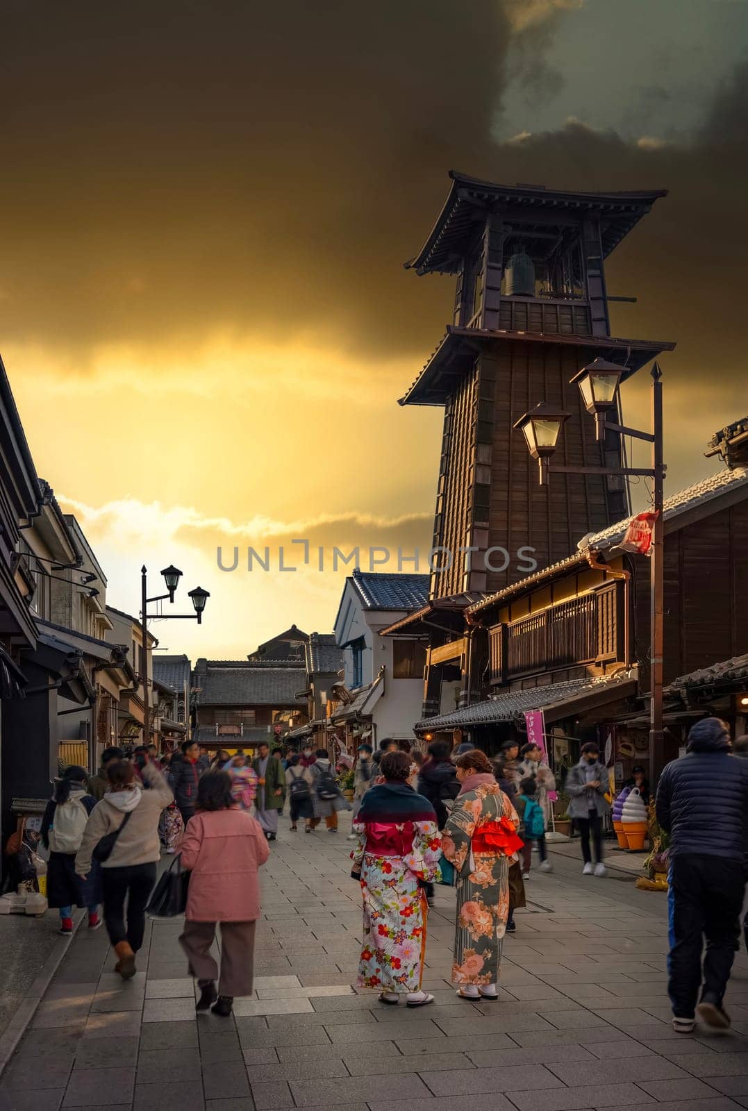 tokyo, japan - dec 31 2022: Tourists in kimono strolling at dusk in Kashiya or Dagashi Yokochô street of Koedo Kawagoe historic district with its landmark Time Bell Tower builded in Kurazukuri style.