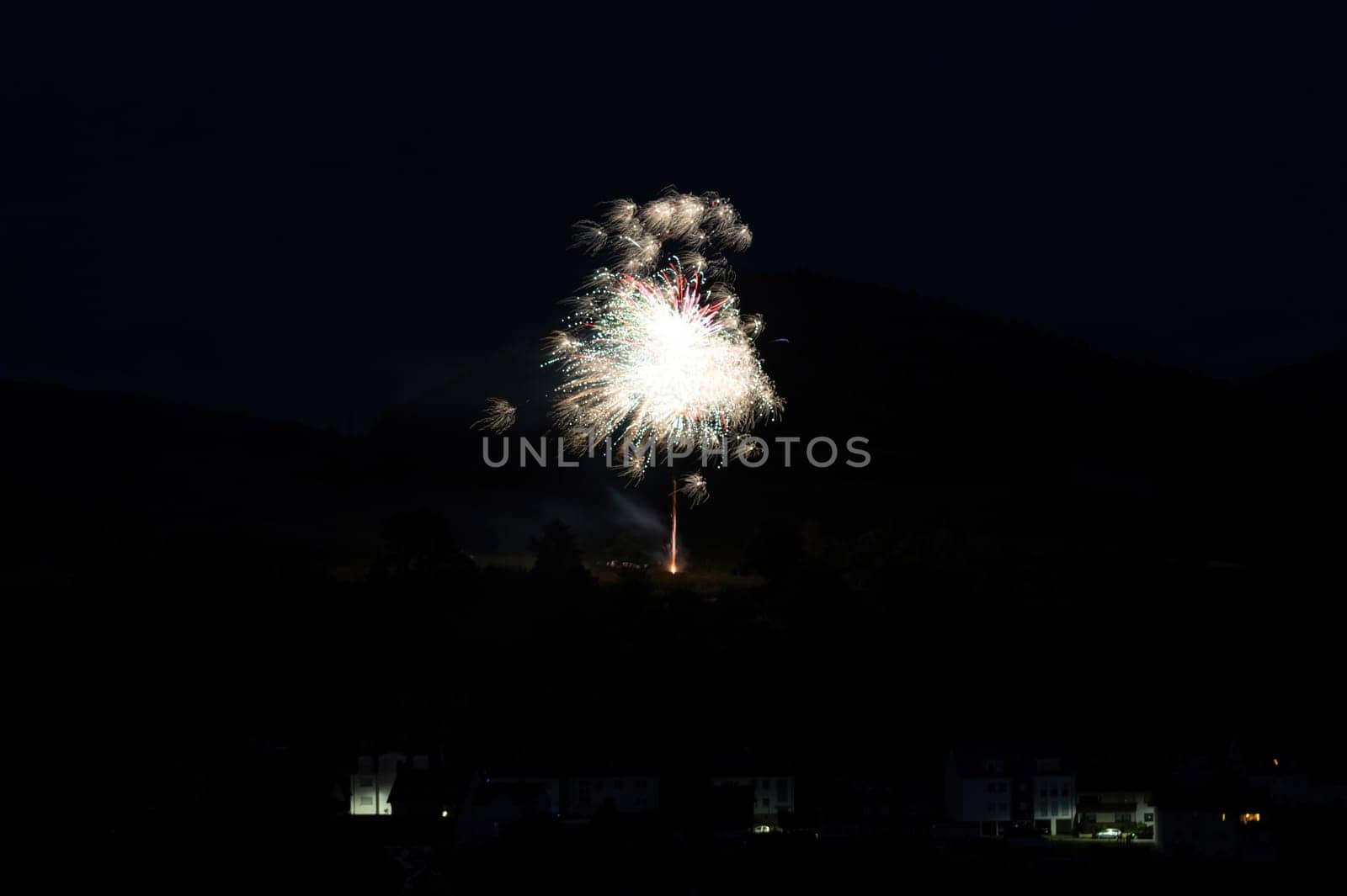 A firework rocket in the sky on a mountain at night, a few illuminated houses in the foreground,A firework rocket in the sky on a mountain at night, a few illuminated houses in the foreground