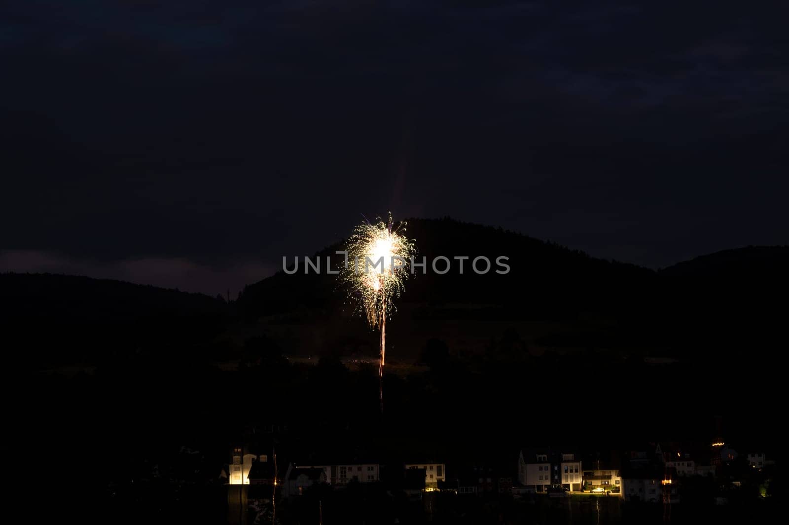 A firework rocket in the sky on a mountain at night, a few illuminated houses in the foreground,A firework rocket in the sky on a mountain at night, a few illuminated houses in the foreground