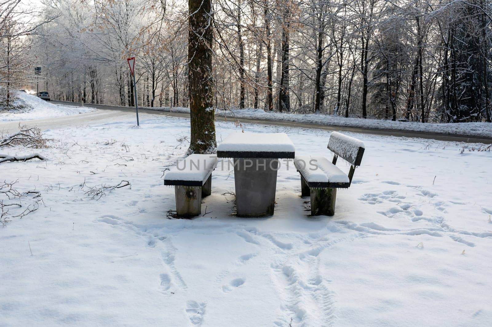 Picnic bench and table in a parking lot in the snow, in a forest