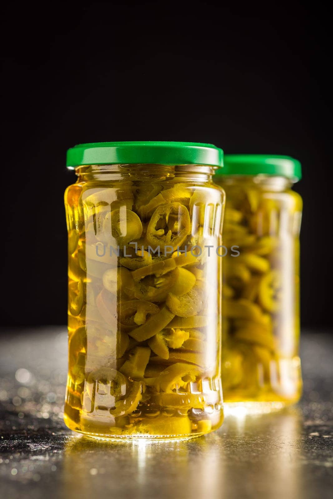Pickled sliced jalapeno peppers in jar on a black table.