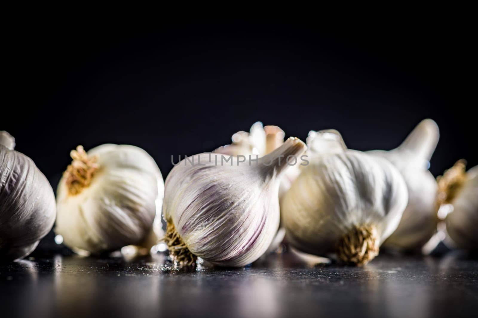 Unpeeled garlic bulbs cloves on a black table.