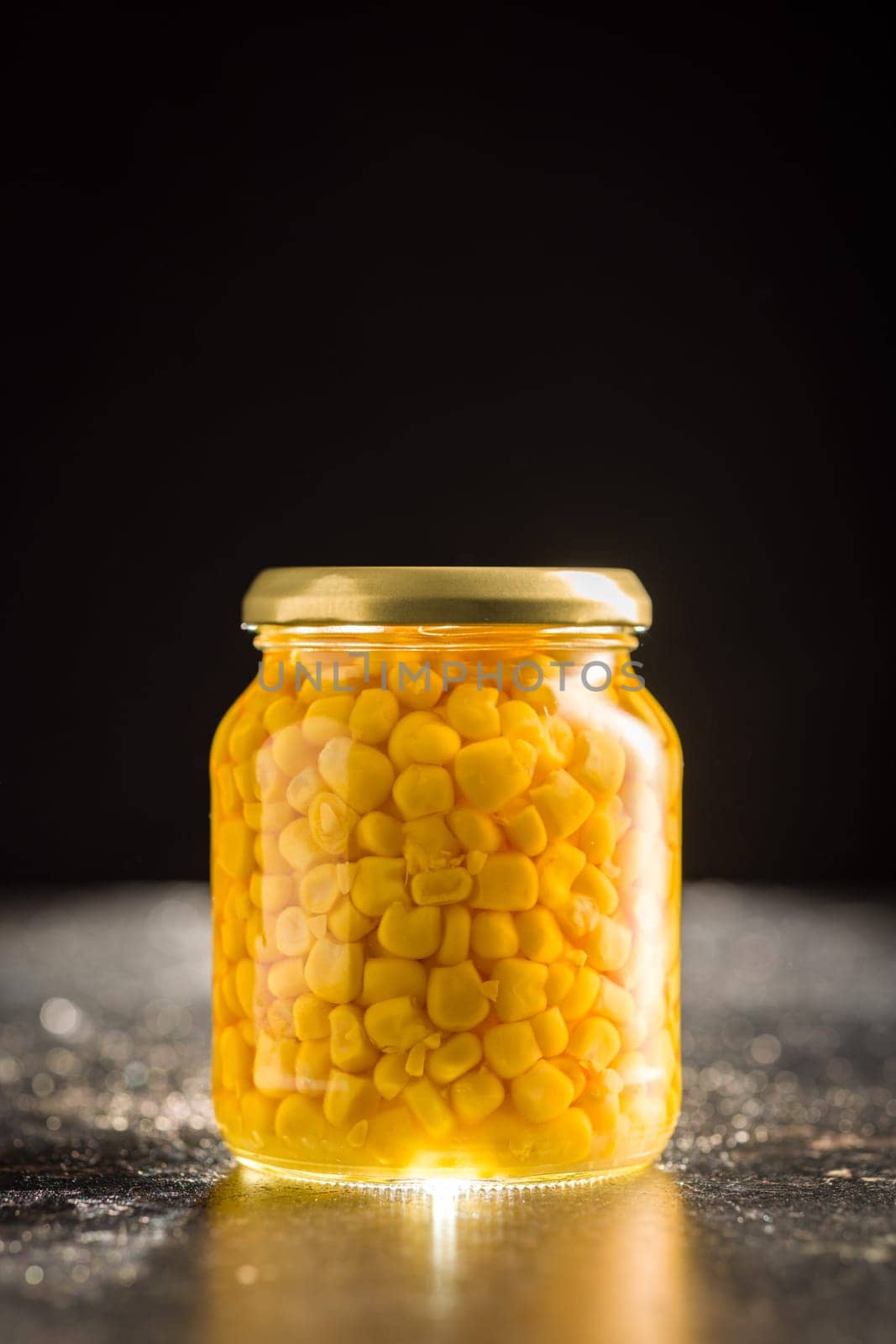 Canned sweet corn in jar on a black table.